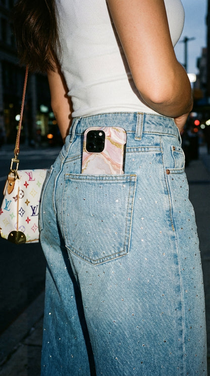 Trendy feminine phone case with pink, gold, and rose gold marble pattern tucked into sparkling denim pocket, showcasing a stylish and popular aesthetic vibe.