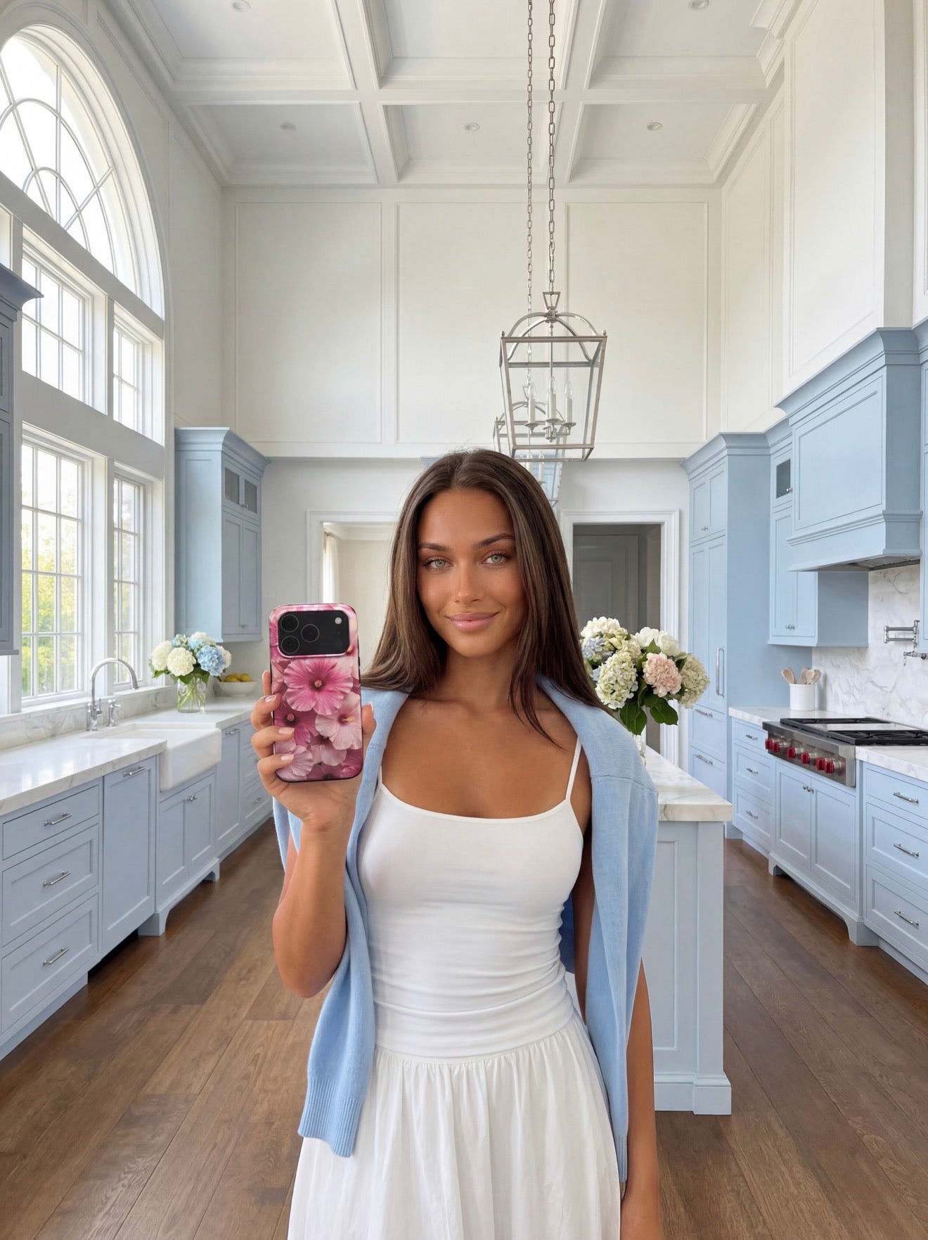 Trendy young woman holding a phone with a pink and red floral phone case in a bright, stylish kitchen setting.