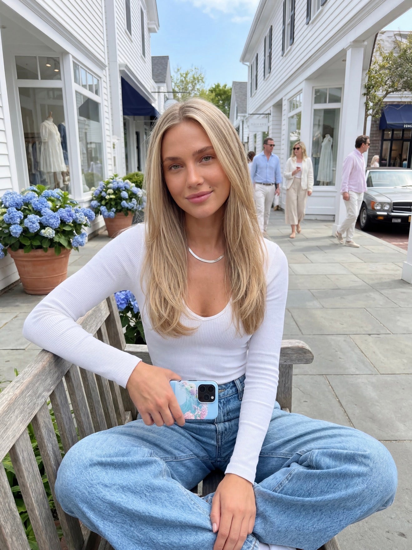 Trendy young woman sitting outdoors holding a colorful pink, blue, yellow, green, and purple phone case, embodying an aesthetic and feminine vibe.