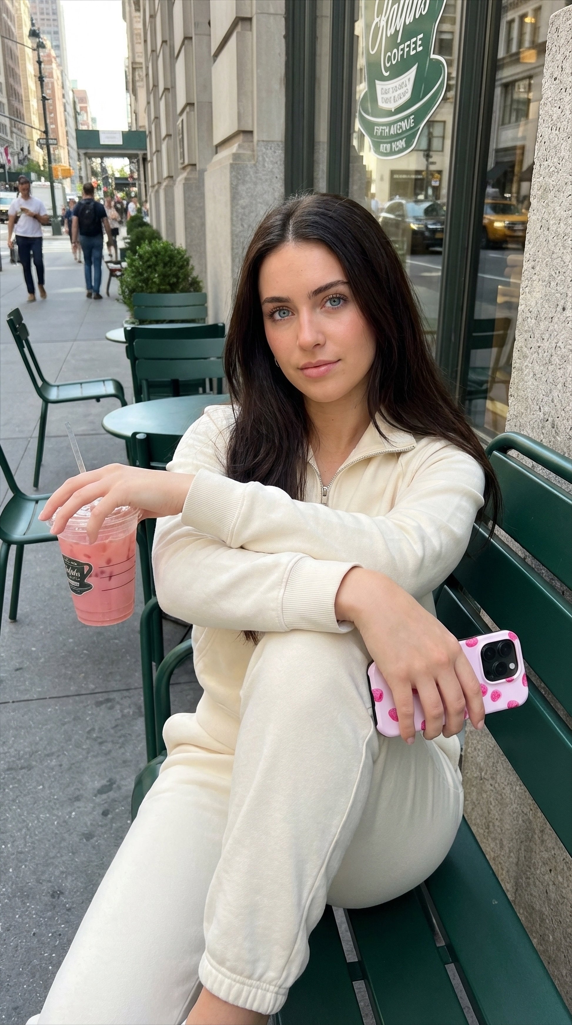 Young woman sitting outdoors holding a trendy pink and red multicolored phone case and a pink drink, showcasing a feminine and aesthetic style.