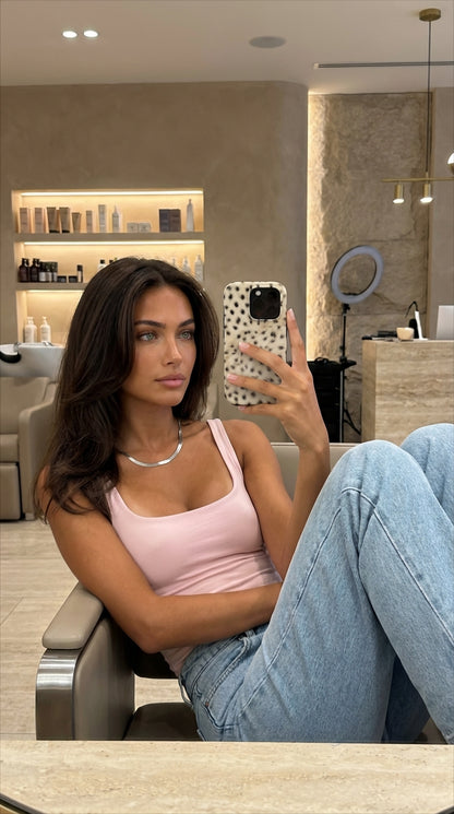 Trendy woman taking a mirror selfie holding a phone with a fluffy, multicolored cheetah pattern case in gold, bronze, brown, beige, and black tones.